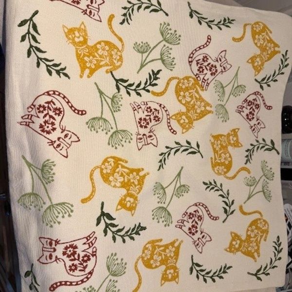 Fabric with yellow and red floral cat patterns and green leafy accents.