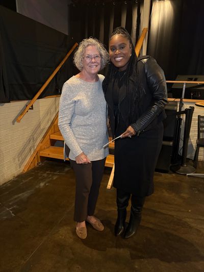 Two women smiling and posing together indoors near stairs.
