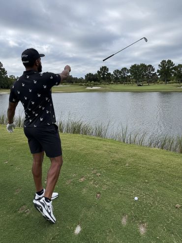 Man throwing a golf club near a water hazard on a golf course.