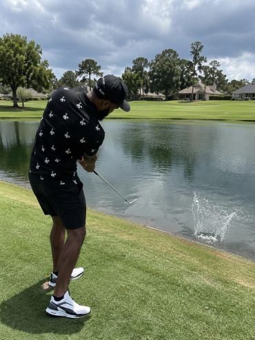 Man hitting golf ball into water on golf course.
