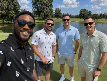 Four men posing on a golf course under blue sky.