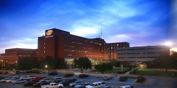 A hospital building at dusk with a parking lot in the foreground.