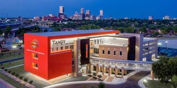 Modern Oklahoma State University building with city skyline in the background at dusk.