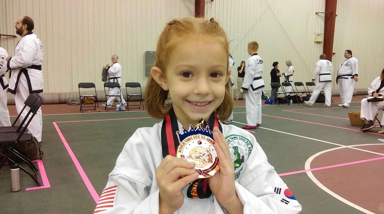 Young girl smiling with a Taekwondo medal indoors.