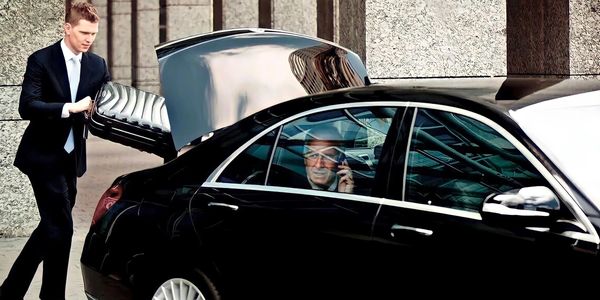 A professional chauffeur putting luggage in a limousine in front of Houston Airport