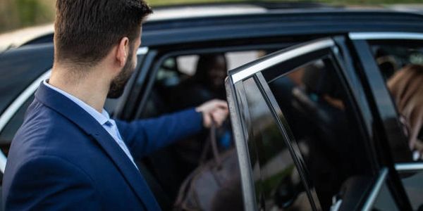 A smiling chauffeur assisting with luggage into a limousine in front of Houston Airport
