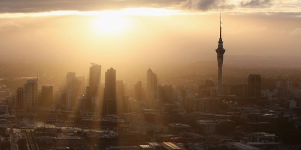 Sunset casting golden rays over a city's skyline with a prominent tall tower.