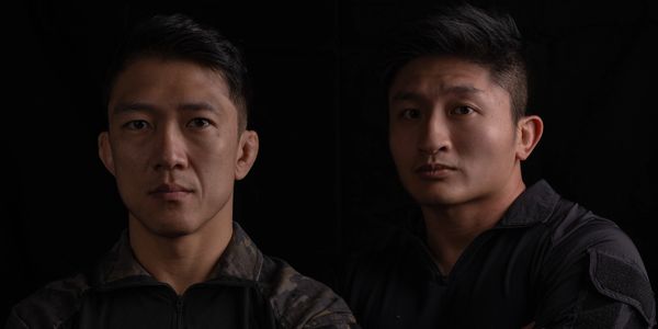 Two serious men in dark clothing against a black background.