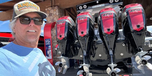 Man in sunglasses and cap takes a selfie with a boat's four large outboard motors.