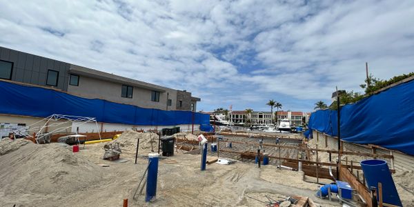 Construction site near waterfront with blue protective barriers and partly cloudy sky.