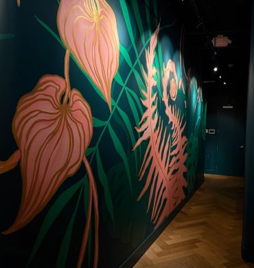 Wall mural with large tropical leaves in pink and green.
