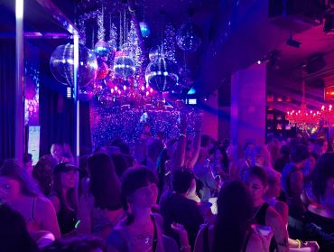 Crowded nightclub with disco balls and vibrant lighting.