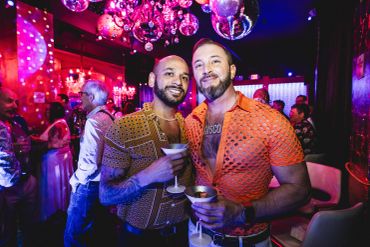 Two men smiling and holding drinks at a vibrant party.