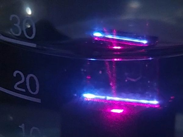 Close-up of glowing blue and pink light inside a transparent container with measurement markings.