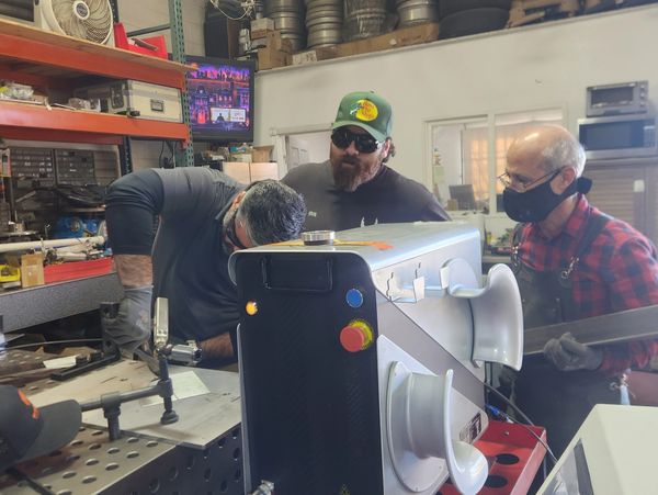Three men working together on a metal project in a workshop.