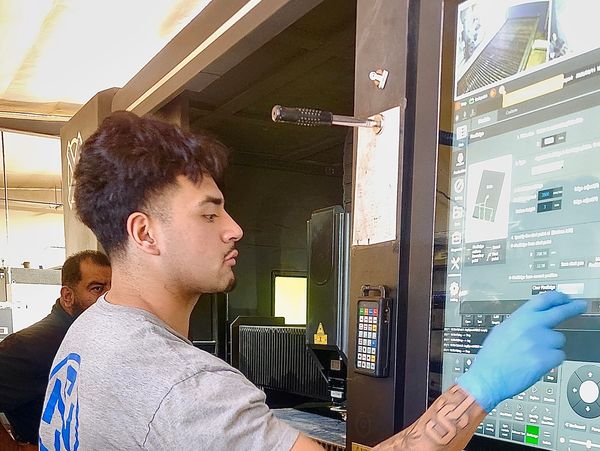 Young man operating a touchscreen industrial machine wearing a blue glove.
