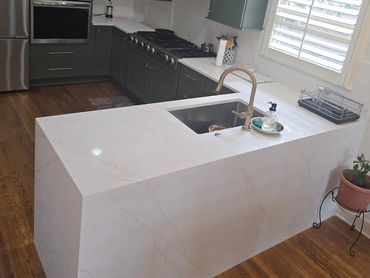 Modern kitchen with green cabinets and marble countertops.