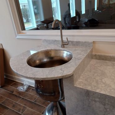 Modern marble countertop with a round metallic sink and faucet.