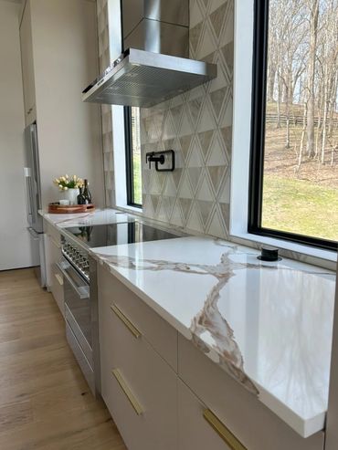 Modern kitchen with marble countertop and large windows overlooking trees.
