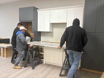 Three workers installing a kitchen countertop in a partially finished kitchen.