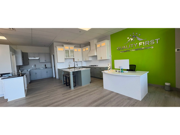 Modern showroom with kitchen displays and a bright green wall featuring the Quality First Granite Countertops logo.