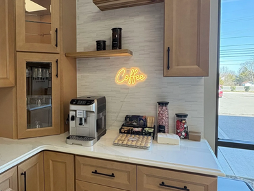 Cozy coffee corner with a machine and treats under a glowing neon "Coffee" sign.