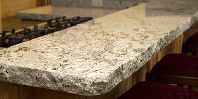 Close-up of a textured granite kitchen countertop with bar stools.