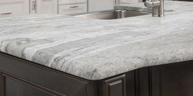 Close-up of a kitchen island with a marble countertop and dark wood cabinetry.