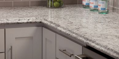 Modern kitchen corner with granite countertop and white cabinets.