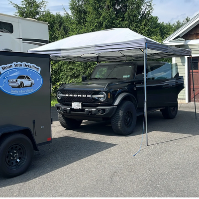 Black Bronco parked under a white canopy near a Moon Auto Detailing trailer.