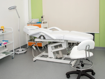 Modern medical examination room with white adjustable examination table and stool.