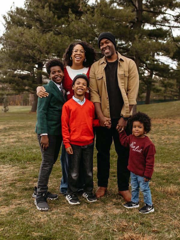 Smiling family of five posing outdoors with trees in the background.