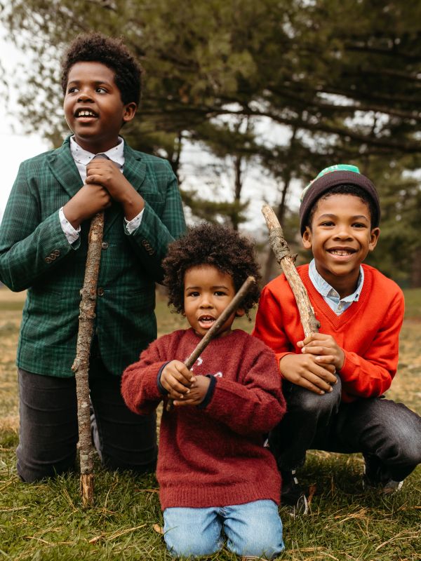 Three boys holding sticks outdoors with cheerful expressions.