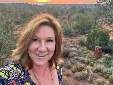 Woman smiling outdoors with a colorful sunset in the background.