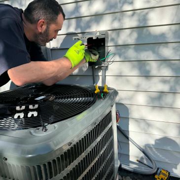 Technician wearing green gloves repairs outdoor AC unit wiring.