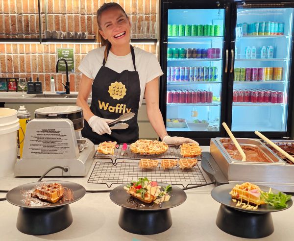 Smiling woman serving waffles at a waffle shop counter.