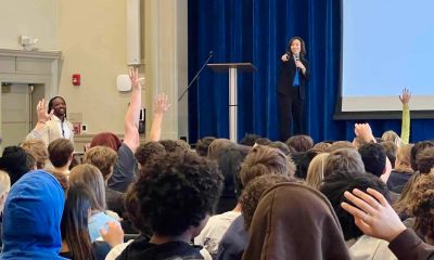 A speaker engaging an audience raising hands in a conference room.