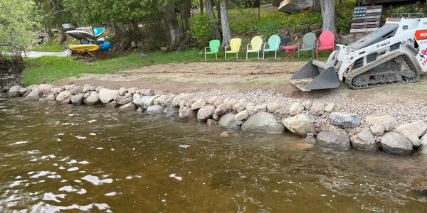 Rock-lined shoreline with colorful chairs and digging machine.