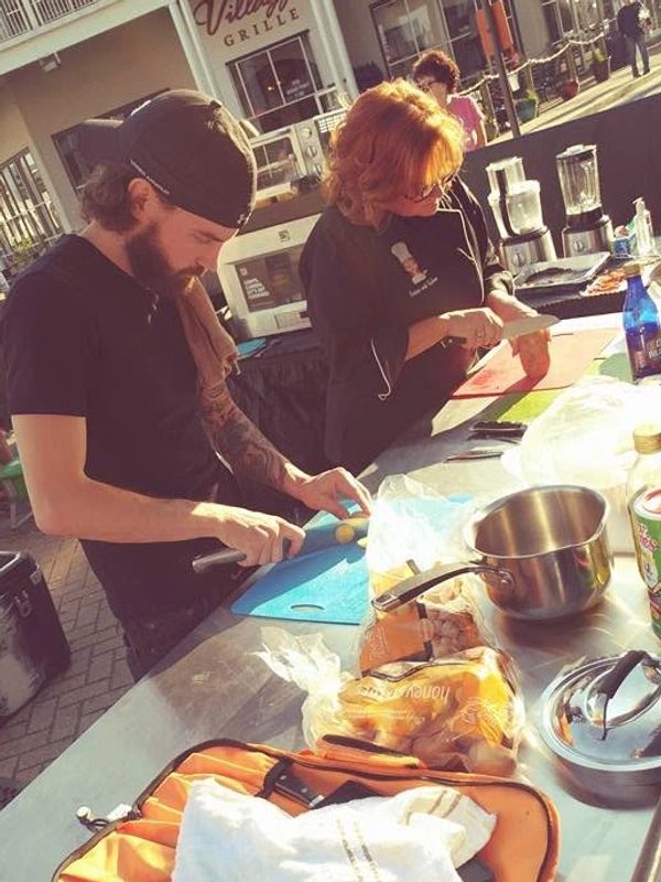 Two people chopping vegetables at an outdoor cooking event.