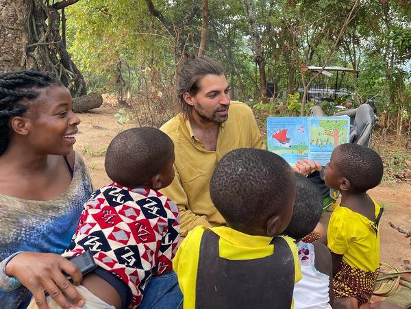 Two adults reading a colorful book to children outdoors.