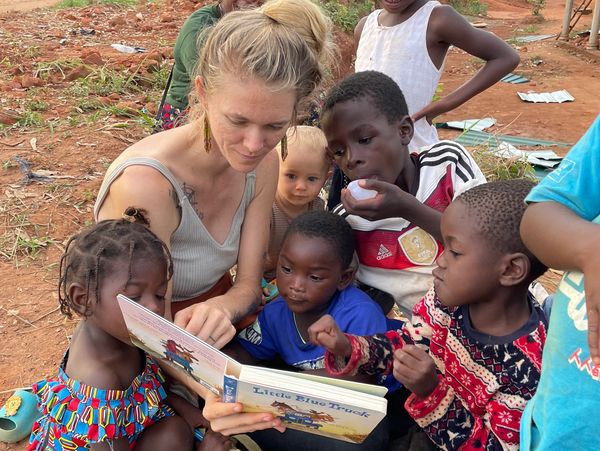 Woman reading a book to children outdoors.