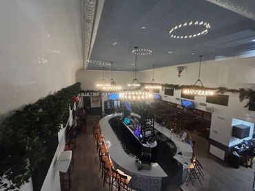 Modern bar with circular chandeliers and a long white counter with stools.