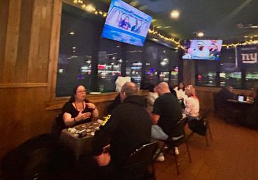 People chatting in a dimly lit bar with sports TVs and fairy lights.