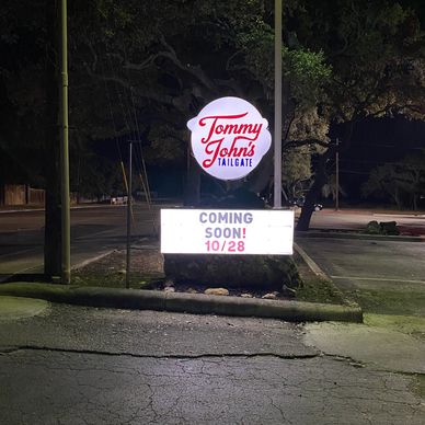 Tommy John's Tailgate sign announcing opening date at night.