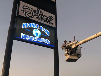 Two workers in a bucket lift fixing a sign at dusk.