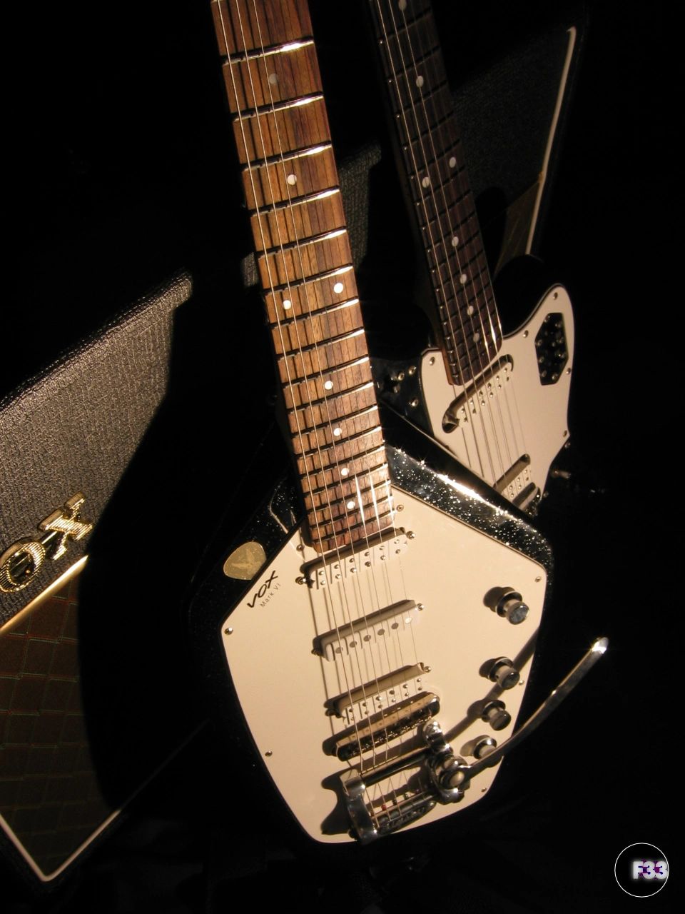 Two electric guitars with a Vox amplifier in dim lighting.