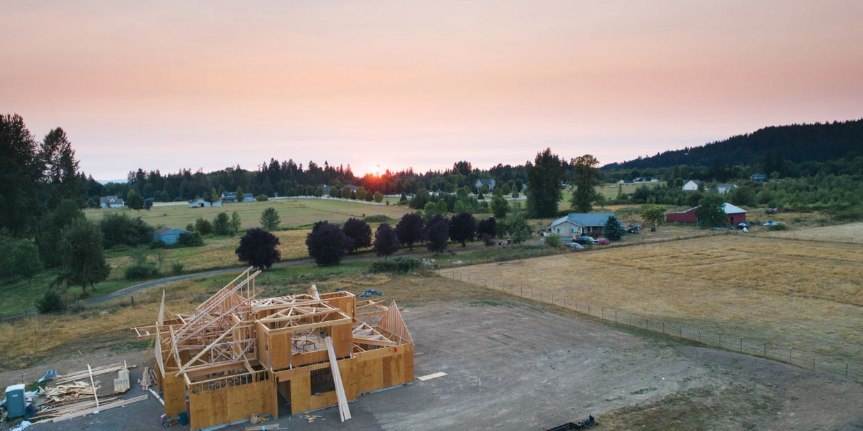 Wooden house framework under construction at sunset in a rural area.