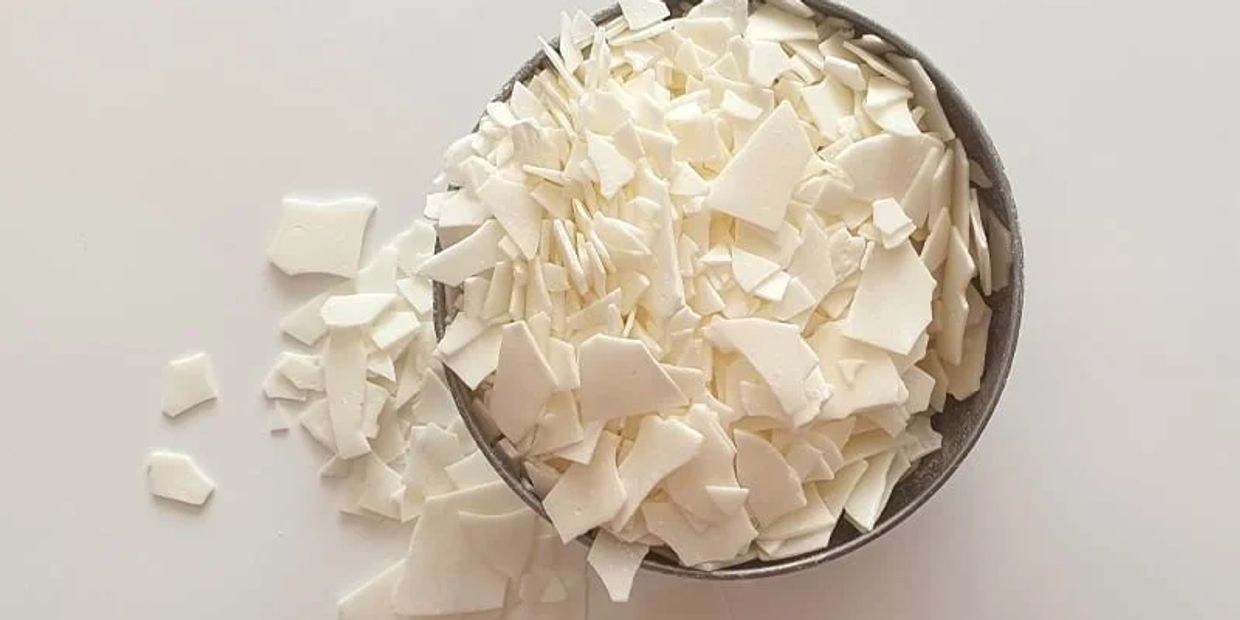 A bowl filled with white soap flakes on a white surface.