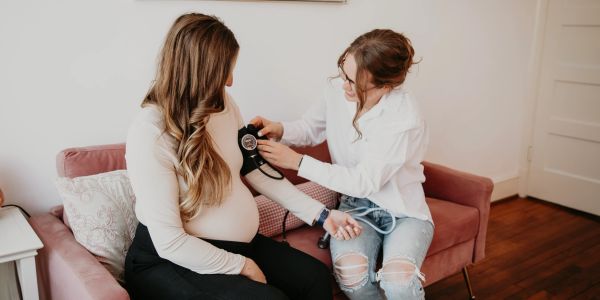 Woman checking pregnant friend's blood pressure at home.