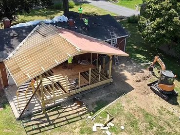 Construction workers building a wooden structure attached to a brick house.